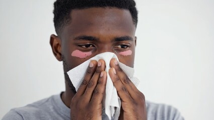 A man in a gray shirt covers his mouth with a white tissue, indicating he is experiencing cold symptoms.