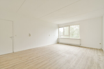 A spacious and bright room with light wooden flooring, white walls, and a large window allowing natural light to fill the space.