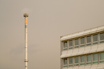 Industrial chimney emitting smoke next to office building