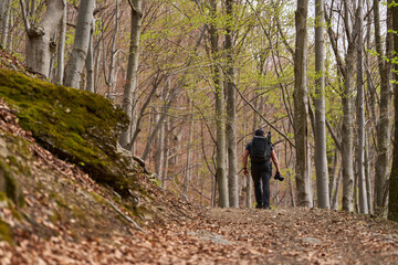 Hiker walking uphill on forest trail with backpack and camera