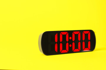 Digital alarm clock showing 10:00 o'clock on yellow background, space for text