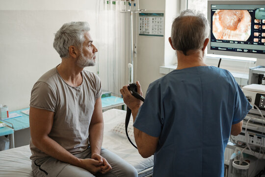 Doctor explaining colonoscopy results to patient using monitor images.