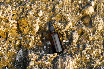 Brown serum jar mockup with dispenser on limestone rock by the sea. Natural cosmetics for skin care...