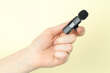 Woman holding lavalier microphone on beige background, closeup