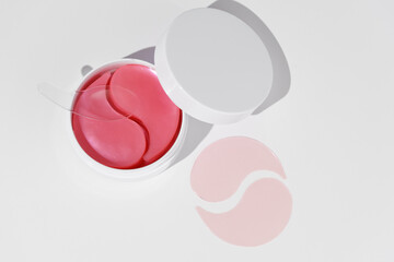 Top view of a white mockup jar featuring pink hydrogel eye patches and a spatula on a white background. Natural hydration, reduces wrinkles, firms the skin, and brightens under-eye circles.