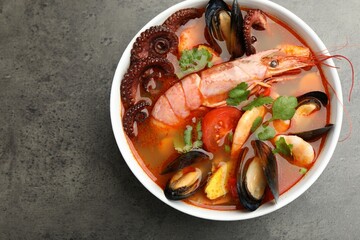 Delicious seafood soup in bowl on gray textured table, top view. Space for text