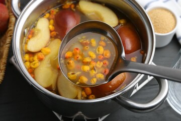 Taking tasty compot with ladle from pot on grey wooden table, closeup