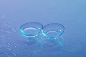 Pair of contact lenses and water drops on color mirror surface, closeup
