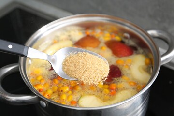 Adding sugar into tasty compot in pot on stove, closeup