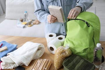 Survival kit. Woman packing different emergency supplies at wooden table indoors, closeup