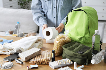 Survival kit. Woman packing different emergency supplies at wooden table indoors, closeup