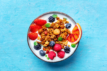 Granola with yogurt and fresh fruit. Organic gourmet muesli with ingredients, overhead flat lay shot on a blue background