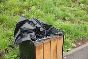 Broken black umbrella in garbage bin outdoors