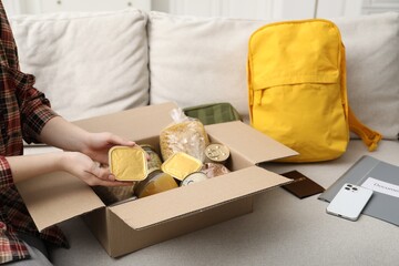 Survival kit. Woman packing different emergency supplies on sofa indoors, closeup