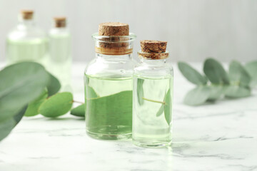 Bottles of essential oil and eucalyptus leaves on white marble table, closeup