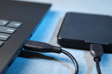 Hard disk drive with USB cable connected to laptop on blue textured table, closeup