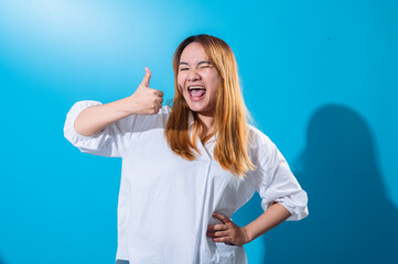 Asian woman with long straight hair wearing white shirt shows enthusiastic thumbs up while smiling...