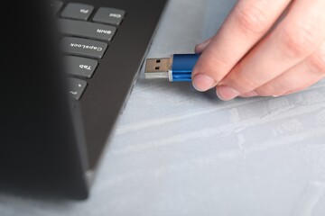 Woman inserting flash drive into laptop at gray textured table, closeup