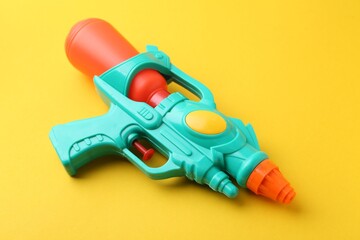Bright plastic water gun on yellow background, closeup