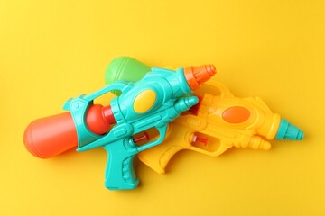 Bright plastic water guns on yellow background, top view