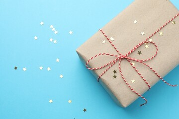 Gift wrapped in kraft paper and confetti on light blue background, top view