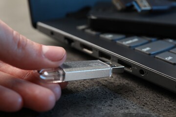 Man inserting modern flash drive at grey table, closeup