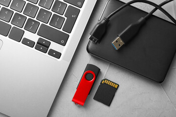 Flash drive, SD memory card, external hard disk and laptop on light grey table, flat lay