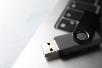 Flash drive and laptop on light grey table, closeup