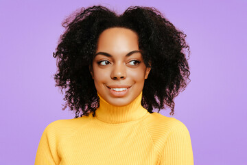 Smiling African American woman with natural curly hair, wearing a yellow turtleneck sweater, glancing sideways with a playful, mischievous expression against a soft purple background.