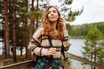 Young woman with backpack hiking on wooden paths in forest. Beautiful female traveler feeling freedom and enjoying lake view. Hiking, nature concept.
