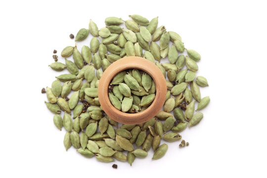 A mud pot filled with organic Cardamom (Elettaria cardamomum) is placed on a heap of whole cardamom, isolated on a white background.