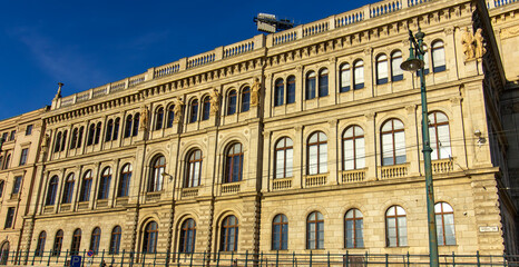 Facade of historic neoclassical building with arched windows and sculptures in Budapest, Hungary, illuminated by warm sunlight under clear blue sky