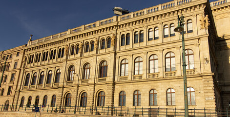 Facade of historic neoclassical building with arched windows and sculptures in Budapest, Hungary, illuminated by warm sunlight under clear blue sky