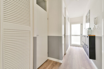 A sleek, modern interior hallway featuring minimalist design, light-colored walls, and natural light streaming through a large window.