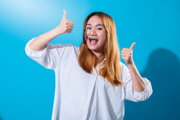 Asian woman with long straight hair in white shirt smiles and enthusiastically gives double thumbs...