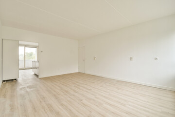 Spacious, empty room featuring light-colored wooden flooring and white walls, creating a serene and minimalist aesthetic with natural light flowing through the windows.