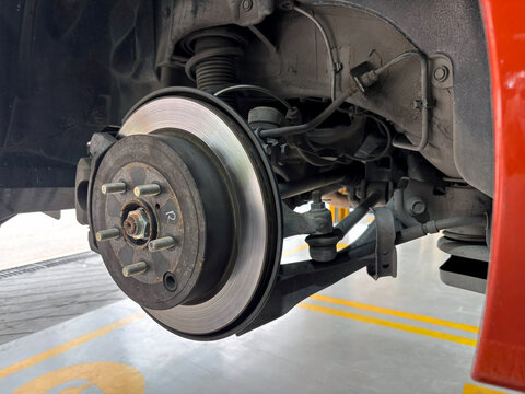 A car's brake assembly is under inspection at an auto repair facility. The technician assesses the brake disc, caliper, and suspension component for any need repair.
