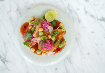 A beautifully arranged dish feature fresh fish topped with colorful ingredients like herb and pickled onion, served with lime on a sleek marble table.