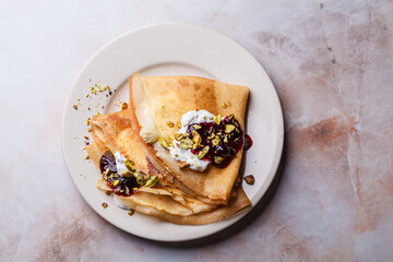 Breakfast crepes with sour cream, jam and pistachio.