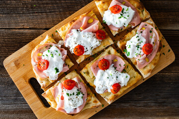 Pinsa Romana with boiled ham, burrata cheese and cherry tomatoes on wooden table	