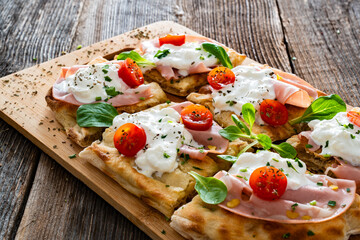 Pinsa Romana with boiled ham, burrata cheese and cherry tomatoes on wooden table	