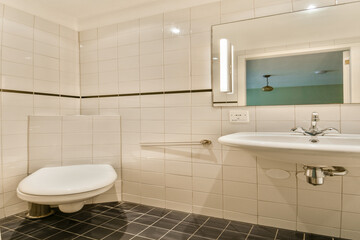 A contemporary bathroom featuring white ceramic tiles, a sleek sink, and an elegant mirror. The design highlights a minimalist aesthetic with soft lighting.