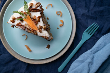 Slice of delicious carrot cake topped with cream cheese frosting, pecan pieces, and shaved carrot...