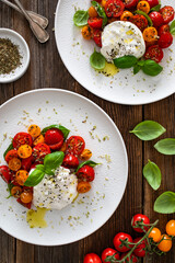 Caprese salad -  cherry tomatoes, fresh basil leaves and burrata cheese on wooden background