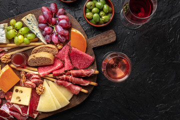 Antipasti or tapas. Charcuterie and cheese platter with wine, Italian or Spanish food and drinks, on a black slate background with copy space