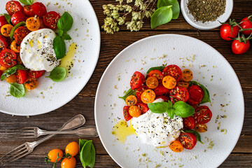 Caprese salad -  cherry tomatoes, fresh basil leaves and burrata cheese on wooden background