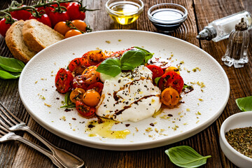 Caprese salad -  cherry tomatoes, fresh basil leaves and burrata cheese on wooden background