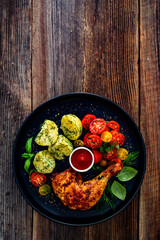 Oven roasted chicken leg with boiled potatoes, fresh tomato salad and ketchup on wooden table	