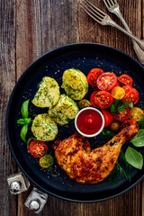 Oven roasted chicken leg with boiled potatoes, fresh tomato salad and ketchup on wooden table	