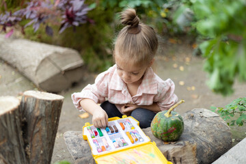 Top view of girl enjoying art and craft drawing in the garden on pumpkin. Children drawing with...